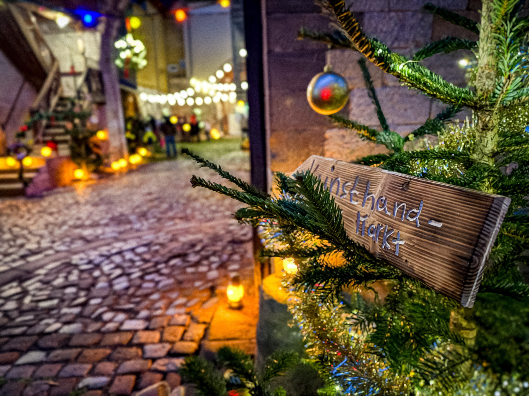 Einzigartig illuminierter Adventsmarkt mit Weg aus Kopfsteinpflaster, festliche Dekoration durch Tannenzweige und Lichterketten.