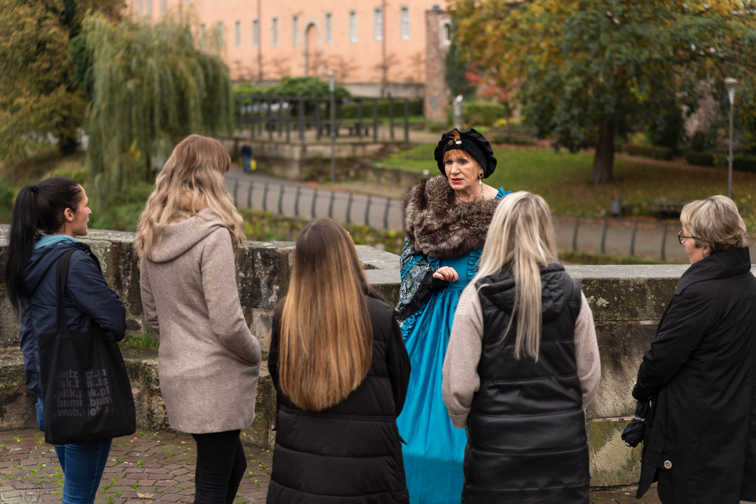 Eine Frau in historischem Kostüm führt eine Gruppe auf einer Stadtführung im Freien an.